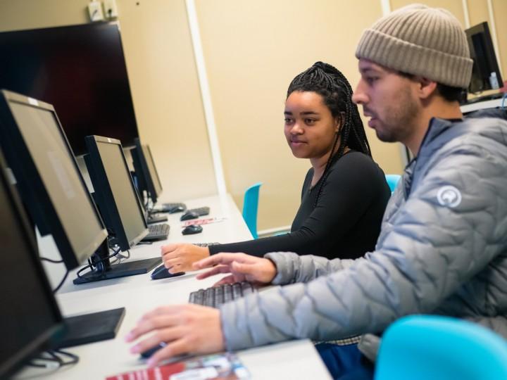 Two students sit together at computer during class